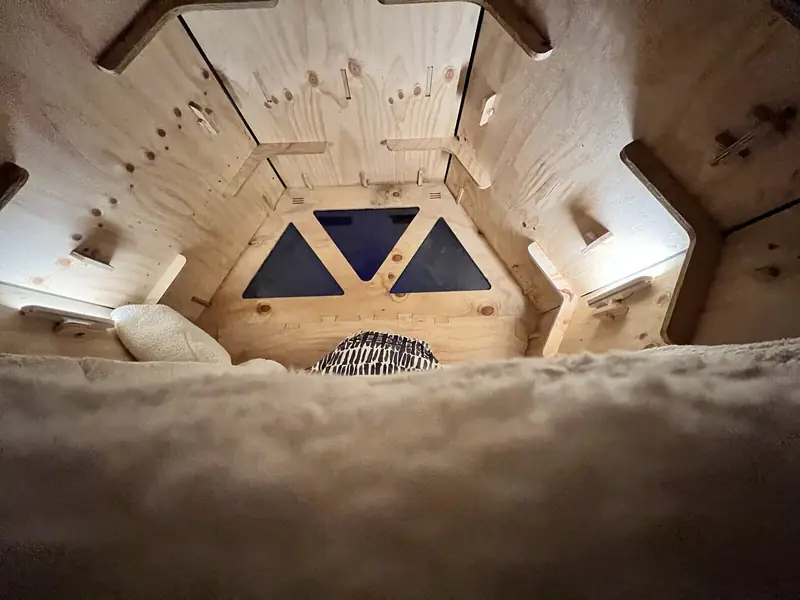 La cama con cobertor de piel sintética, bajo las ventanas triangulares