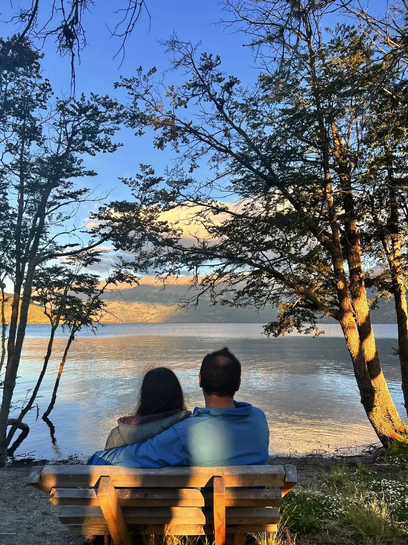 Dos personas en una banca, mirando el lago al atardecer