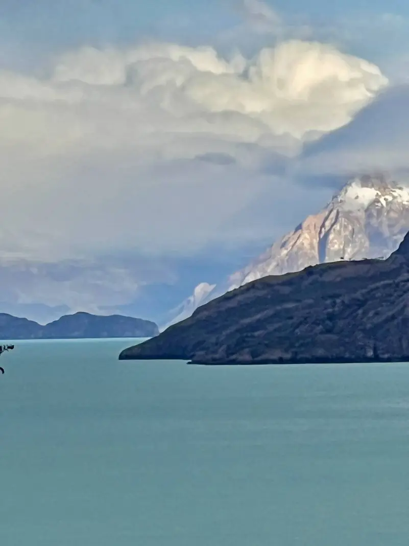 Un cerro nevado entre las nubes, sobre el lago